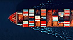 Aerial view of a cargo ship carrying colorful containers, cutting through deep blue waters with visible wave patterns.