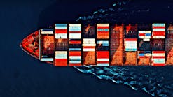 Aerial view of a cargo ship carrying colorful containers, cutting through deep blue waters with visible wave patterns.